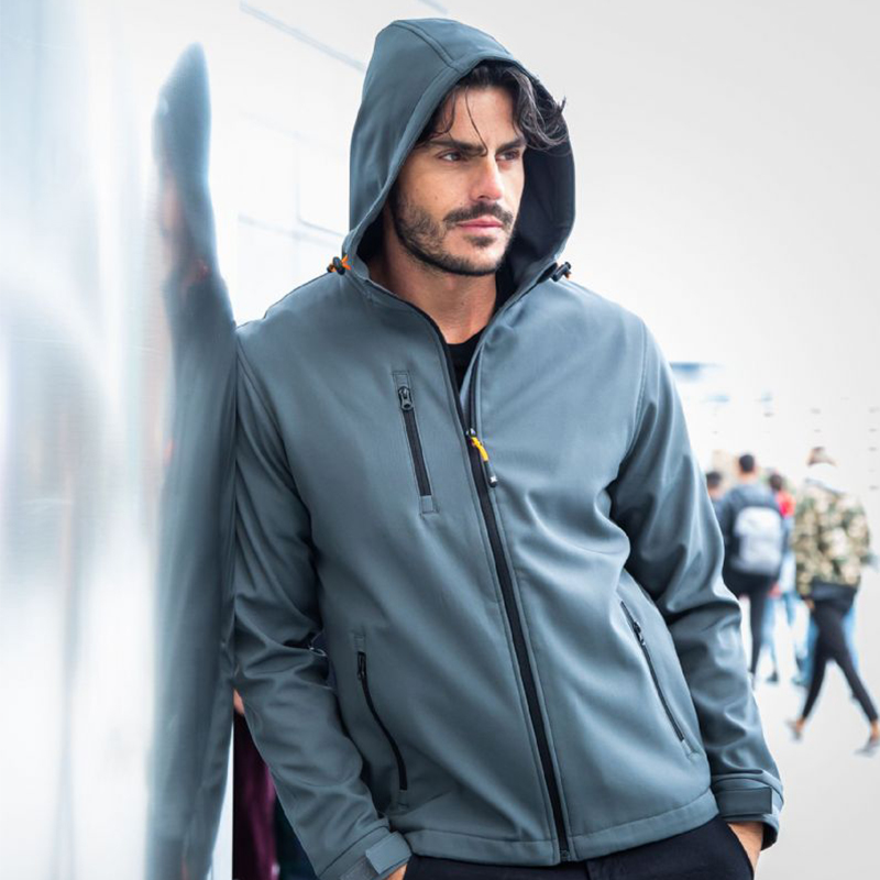 Modello indossa la giacca softshell Innsbruck grigia con cappuccio e zip a contrasto, dettaglio del tessuto tecnico e della vestibilità.