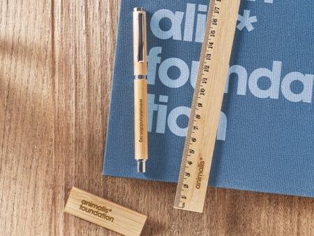 Set di Gadget in bambù promozionali Animalis Foundation: penna, righello e chiavetta USB su quaderno blu.