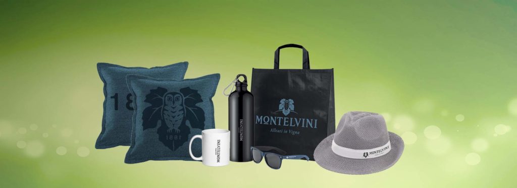 Selezione di gadget personalizzati Montelvini: cuscini, borracce, tazze, shopper, occhiali da sole e cappelli con logo aziendale.