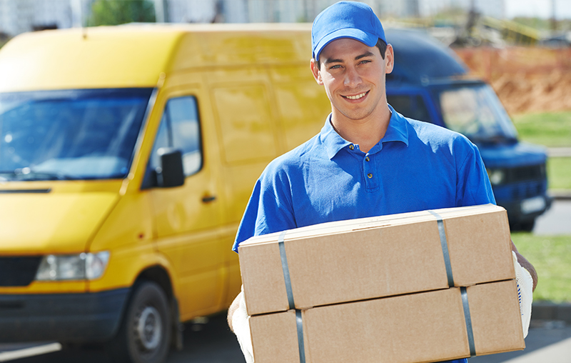 Corriere sorridente con divisa blu che consegna pacchi davanti a un furgone giallo per servizi di spedizione Pro&Motion.